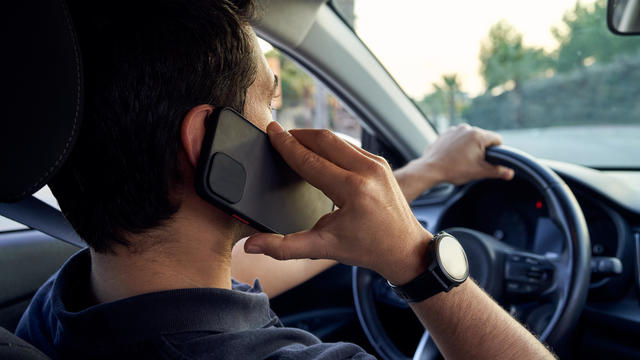 Rear view of a young unrecognizable Hispanic man talking on a smartphone while driving his car. 