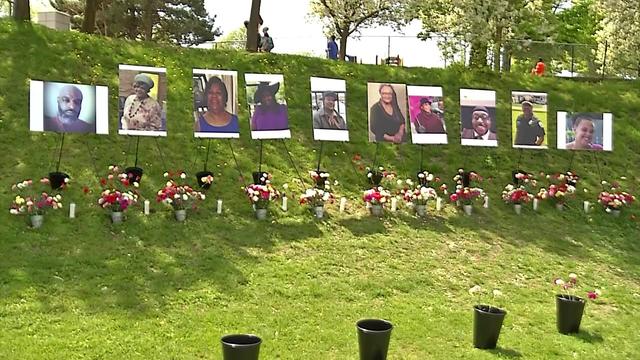Photos of the 10 Buffalo mass shooting victims are displayed on stands in a grassy area with vases of flowers. 