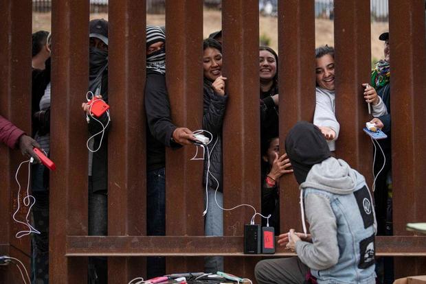 Asylum seekers hold their phones through the border wall as 