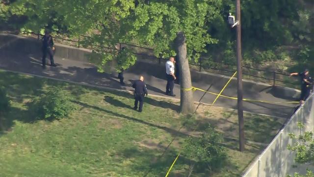 An aerial shot of police officers searching a grassy area and a road blocked off by crime scene tape. 