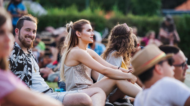 Group of young friends sitting on ground at summer festival. 