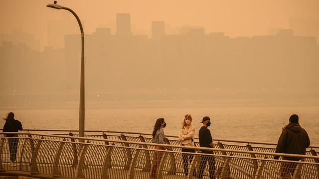 The Manhattan skyline is seen past people wearing face masks while walking along a pier as smoke from wildfires in Canada cause hazy conditions in New York City on June 7, 2023. 