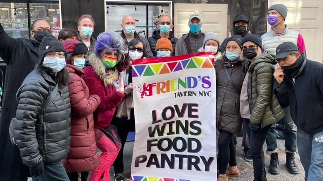 Volunteers with the Love wins Food Pantry stand outside Friend's Tavern holding a banner.