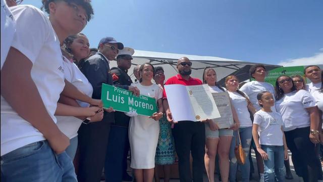 Family, friends and officials pose with a street sign reading "Private First Class Luis Moreno Way." 