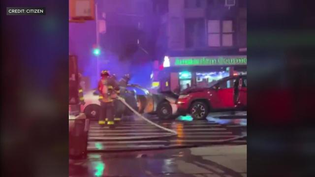 Firefighters hose off an unmarked police car that has crashed head-on into a red SUV. 