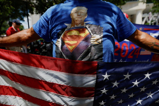 A person wearing a t-shirt depicting former U.S. President Donald Trump holds a U.S. flag as he stands near the Wilkie D. Ferguson Jr. United States Courthouse, in Miami 