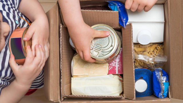 Children opening a food delivery box at home, online ordering. Grocery store delivery. Box full of food in concept donation boxparcel. Delivery during quarantine due to coronavirus COVID-19 disease 