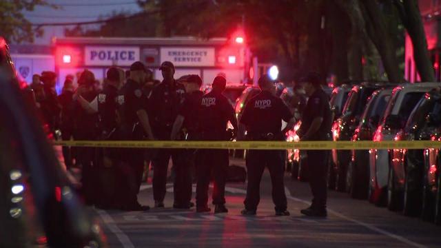 Numerous police officer stand on a street behind crime scene tape. 