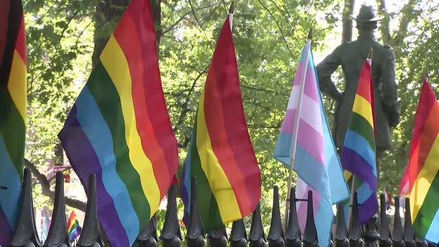 Pride and trans pride flags stand on top of an iron fence at the Stonewall National Monument. 