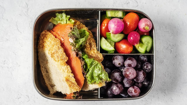 Lunch box with sandwich, vegetables, and fruit on white background 