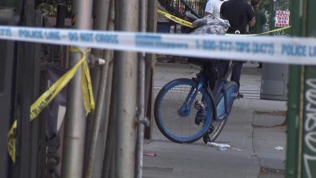 A bicycle stands parked on a sidewalk behind crime scene tape. 