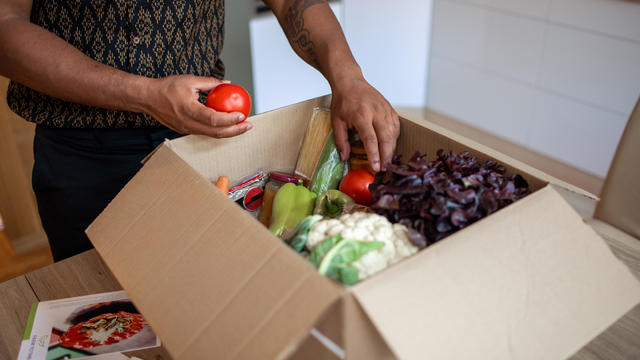 Latin man opening meal kit box full of fresh produce and other ingredients 