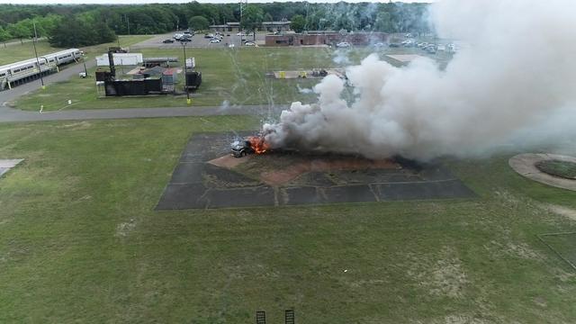 An aerial view of a vehicle that is on fire and billowing smoke after fireworks were set off. 