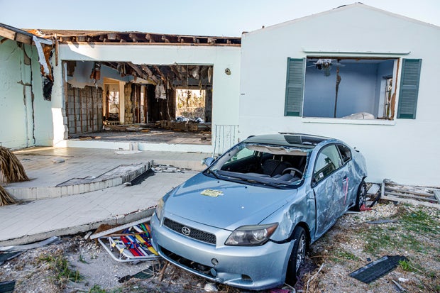 Blue sedan in front of damaged home