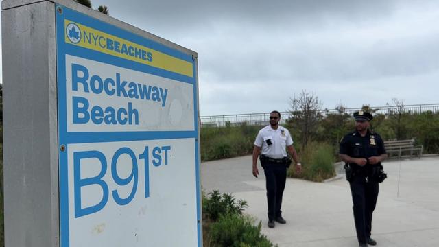 Two NYPD officials walk past a sign for Rockaway Beach at Beach 91st Street. 