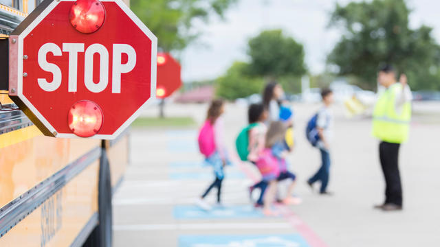 Lights flash on a school bus stop sign as children cross street 