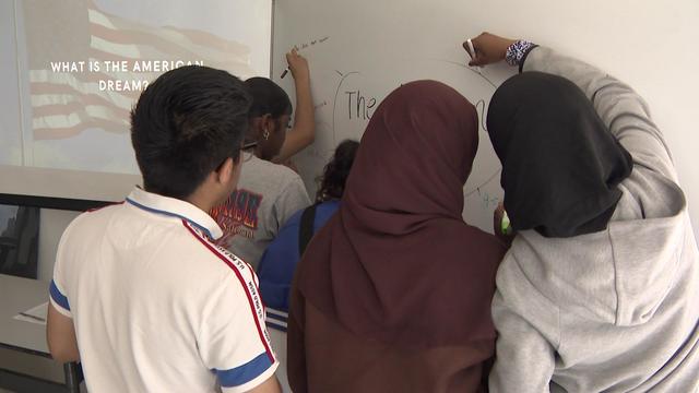 Five students write on a white board with the words "The American Dream" written in a circle. 