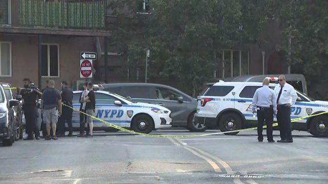 Two NYPD vehicles are parked in an intersection behind crime scene tape. 