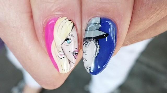 A close-up of custom nail art on a woman's two thumbs -- one nail is pink and has half of Barbie's face; the other nail is blue and has half of J. Robert Oppenheimer's face. 