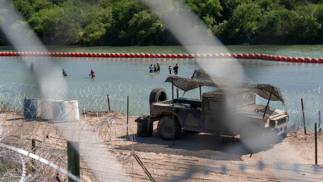 Migrants walk by a string of buoys placed on the water along the Rio Grande border with Mexico in Eagle Pass, Texas, on July 15, 2023, to prevent illegal immigration entry to the U.S. 