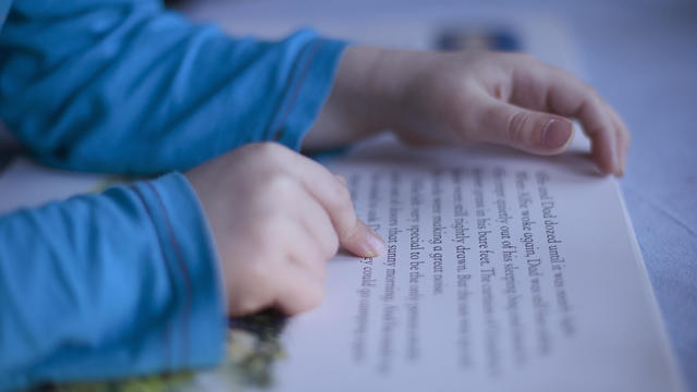 close up boys fingers pointing to words in book 
