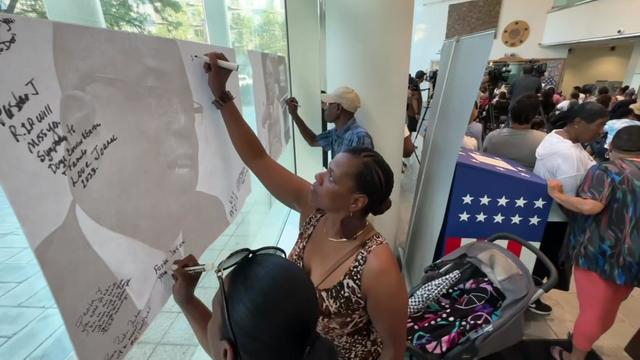 Individuals write messages of tribute on posters with photos of Rev. Dr. Tommie Jackson. 