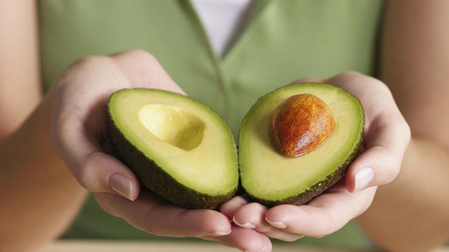 Woman holding halved avocado 