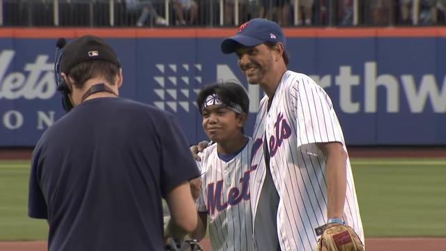 Ralph Macchio stands on the field at Citi Field with his arm around Armaan Mohammed, both wearing Mets jerseys. 