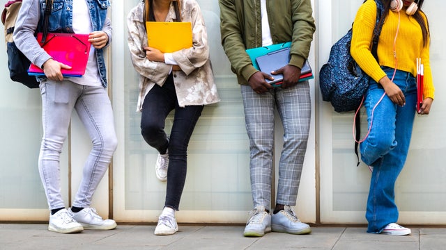Group of multiracial teenage college students ready to go back to school standing against blue background wall. 