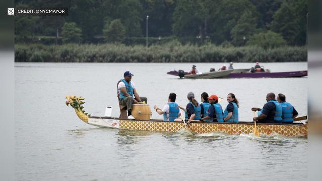 Mayor Eric Adams sits at the head of a dragon boat with rowers. 