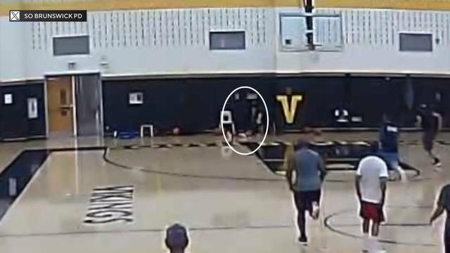 Surveillance footage from inside a gymnasium shows basketball players running towards a man collapsed on the edge of the court. 