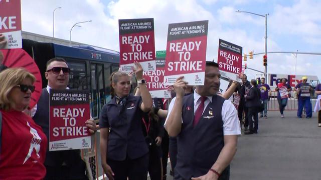 Over a dozen American Airlines flight attendants hold signs reading "Ready to strike" while standing outside LaGuardia Airport. 
