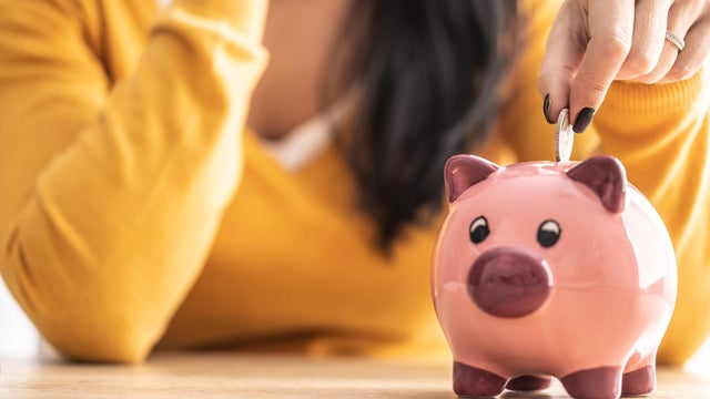 A woman's hand puts a coin into a piggy bank. 
