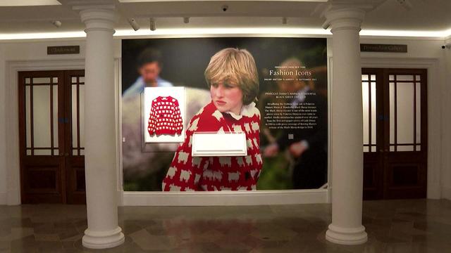 A sweater worn by Princess Diana on display on a wall with a photo of her wearing the sweater. 