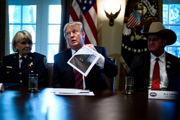 President Donald Trump holds up a photo of a "typical standard wall design" on the 21st day of the partial government shutdown at the White House on Friday, Jan. 11, 2019.