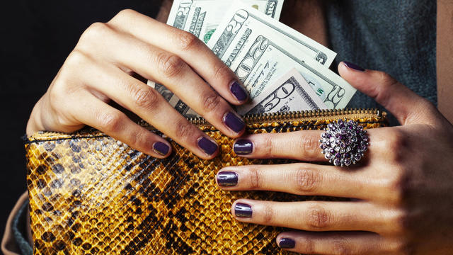 pretty fingers of african american woman holding money closeup with purse, luxury jewellery on python clutch, cash for gifts 