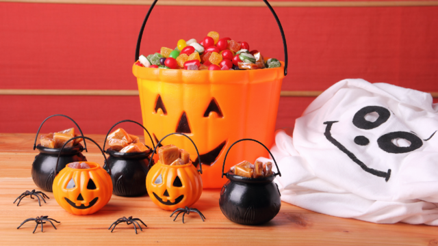 A bucket of Halloween candy surrounded by halloween decorations 