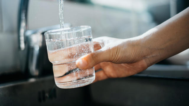 Close up of a woman's hand filling a glass of filtered water right from the tap in the kitchen sink at home 