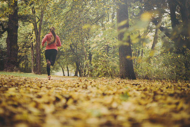 Woman jogging on trail covered in Autumn leaves 