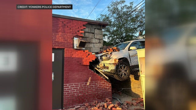 The front of a white vehicle crashed into the corner of a building. 