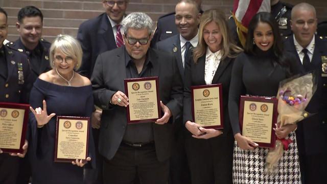 Actor Luis Guzman stands with NYPD members holding plaques. 