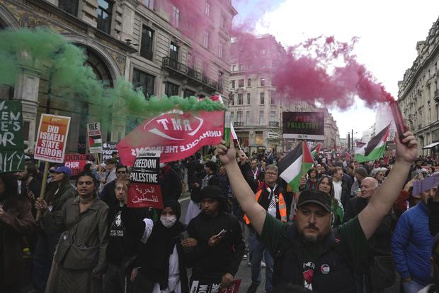 Pro-Palestinian protesters are seen marching in London on October 14, 2023. One protester in the foreground is carrying red and green smoke flares. 