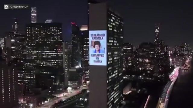 A photo of a woman with the caption "30-year-old Carmilla kidnapped by Hamas" is projected on the side of a building. 