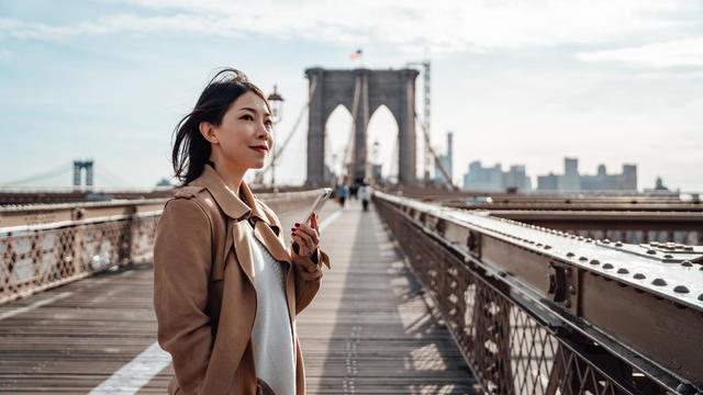 Woman standing on Brooklyn Bridge with smartphone 