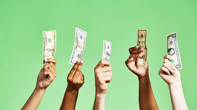 Diverse group of hands holding up US dollar banknotes of various denominations on green background 