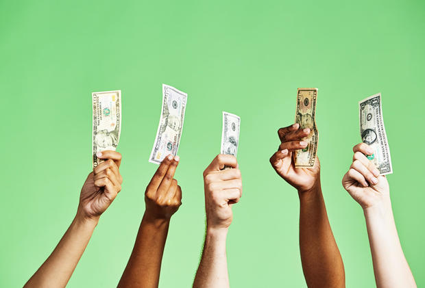 Diverse group of hands holding up US dollar banknotes of various denominations on green background 