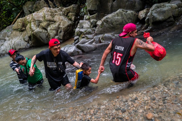 An Ecuadorian migrant family helps each other wade through the river in the wild and dangerous jungle on Nov. 20, 2022, in Darién Gap, Colombia.