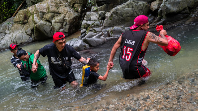 An Ecuadorian migrant family helps each other wade through the river in the wild and dangerous jungle on Nov. 20, 2022, in Darién Gap, Colombia. 