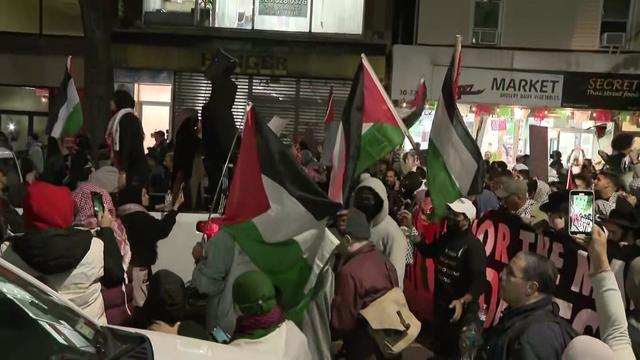 Crowds of people fill a Queens street, many carrying Palestinian flags. 