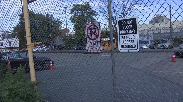 A locked fence outside a parking lot containing multiple vehicles, including two small school buses. 